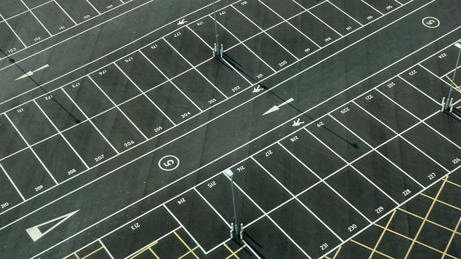 Aerial view of an empty asphalt parking field with numbered stalls, white lane lines and painted directional arrows