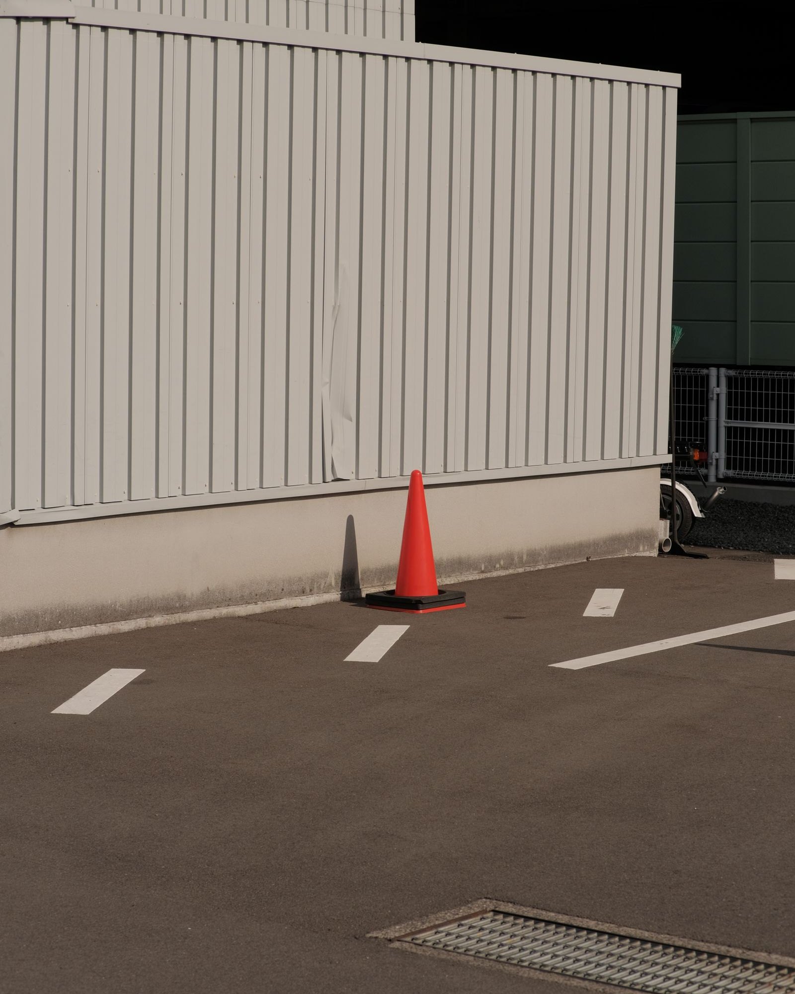 Orange traffic cone at the edge of a marked parking bay against a pale corrugated site wall