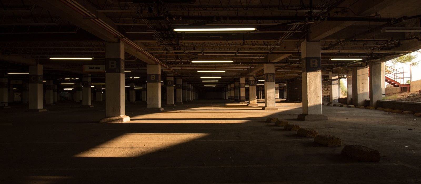 Wide view down a parking structure deck showing lit bays, columns and the exit aperture